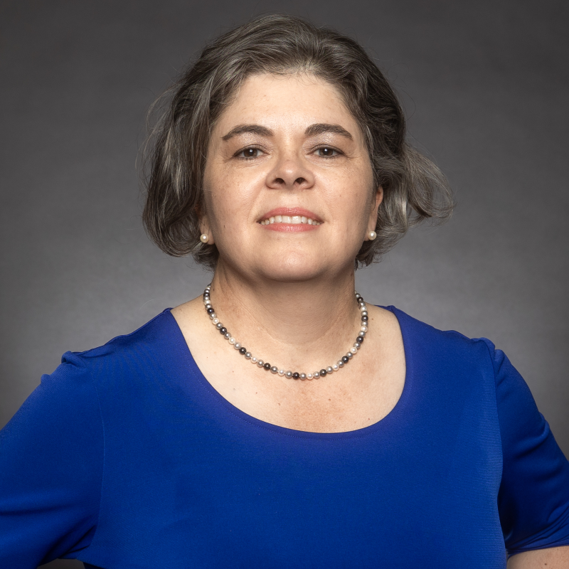 Tonya Jageneaux is wearing a blue shirt and standing in front of a dark grey background. 