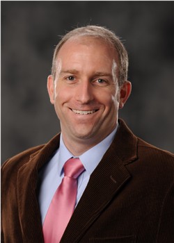 man in suit in front of a grey backdrop - Dan Rice headshot